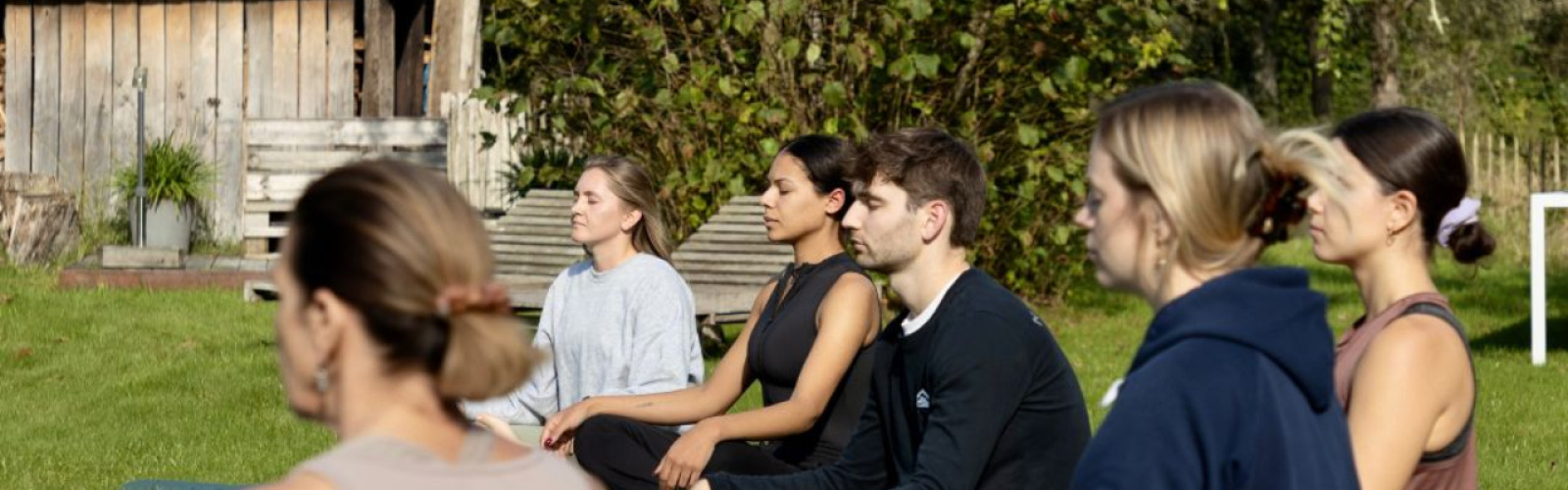 Vrouwen en een man die in kleermakerspositie op het gras zitten.