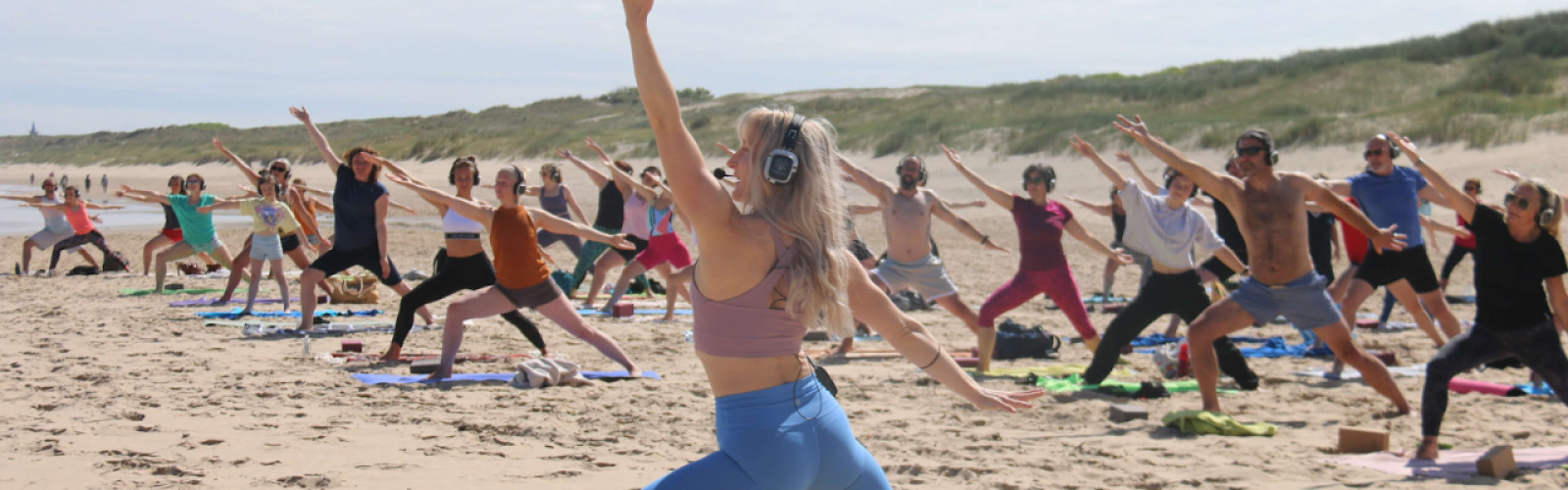 Mensen die op het strand en met een koptelefoon een yoga workshop aan het doen zijn.